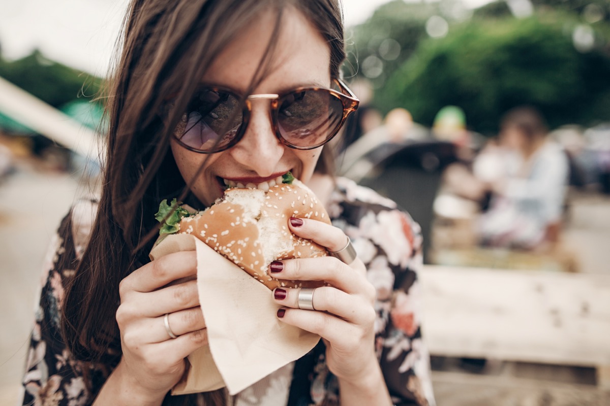 young woman wearing sunglasses eating burger outdoors