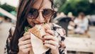 young woman wearing sunglasses eating burger outdoors