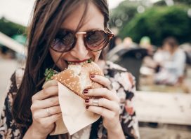young woman wearing sunglasses eating burger outdoors