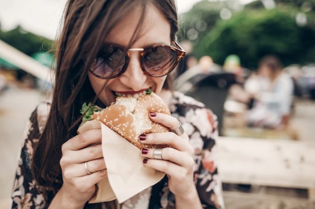 young woman in sunglasses eating burger outdoors