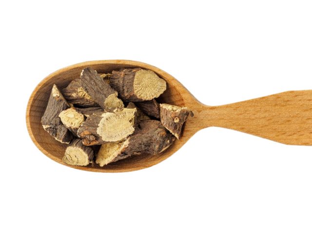 Dry Glycyrrhiza or licorice root in wooden spoon on white background.