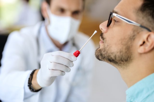 Koronavirüs salgını sırasında doktorun ofisinde PCR testi yaptıran genç adamın yakın çekimi.
