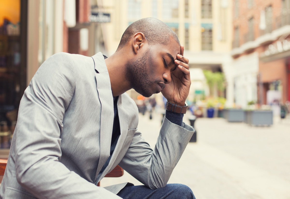 20-or 30-something man in gray blazer and jeans looking depressed outdoors