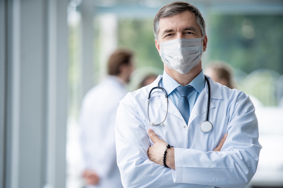 Cheerful mature doctor in face mask posing at camera, healthcare and medicine.