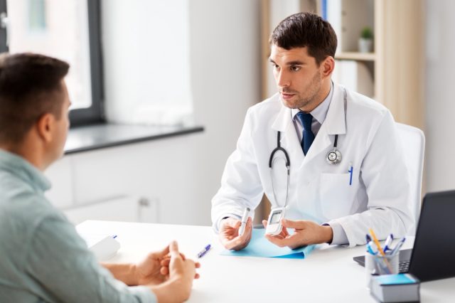 Ein Arzt mit Blutzuckermessgerät und Insulinpen spricht mit einem männlichen Patienten in einer Arztpraxis eines Krankenhauses.