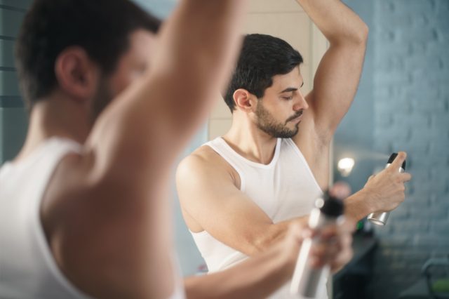 Man using spray deodorant on underarm skin.