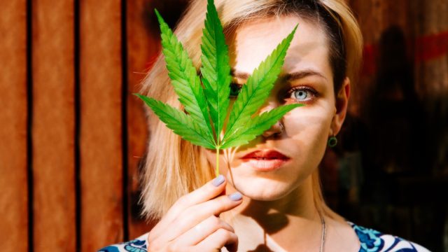 Woman with a cannabis leaf in front of her face.