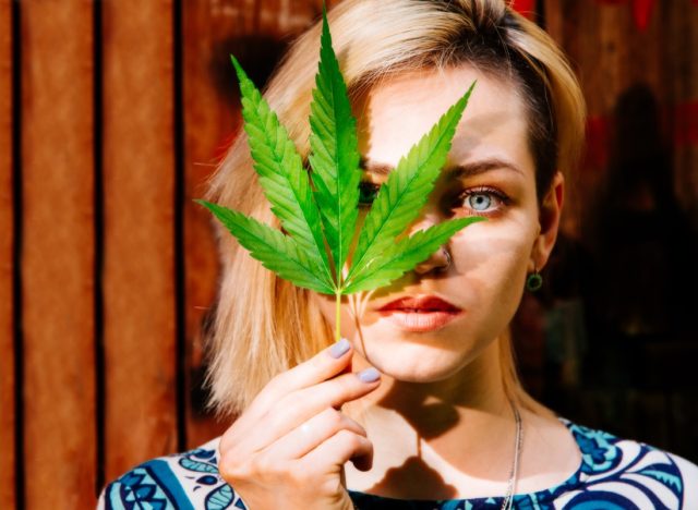Woman with a cannabis leaf in front of her face.
