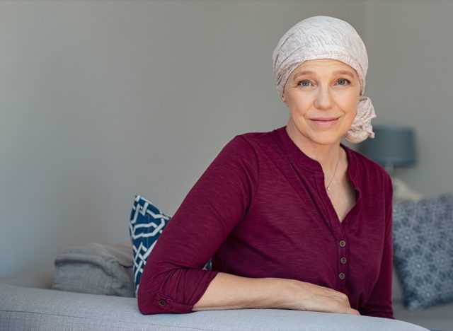 Mature woman with cancer in pink headscarf smiling sitting on couch at home