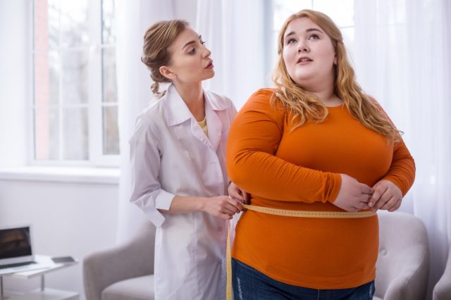 Doctor hablando con una mujer obesa y midiéndola.