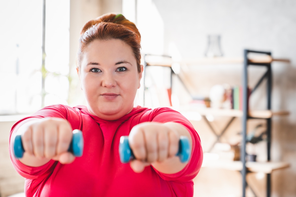 Obese young caucasian woman doing exercise with dumbbells