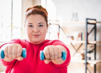 Obese young caucasian woman doing exercise with dumbbells