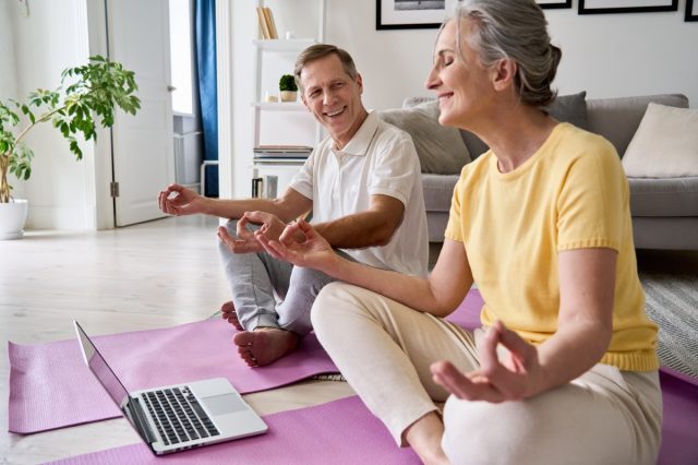 older couple doing yoga in front of a laptop