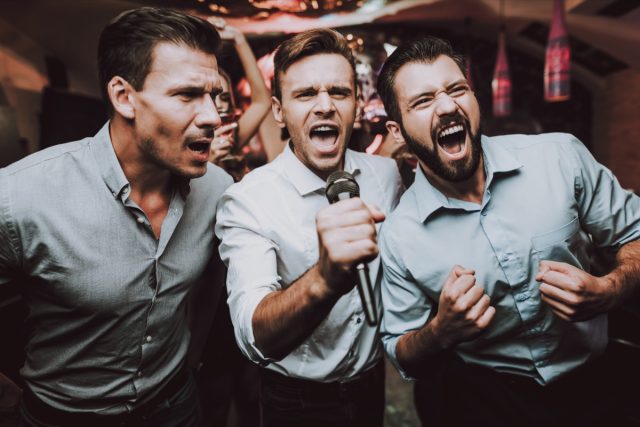 3 hommes chantant du karaoké dans le bar.