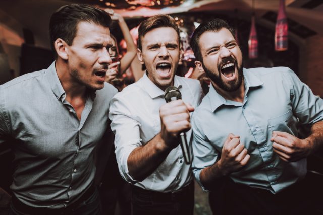 3 men singing karaoke in the bar.