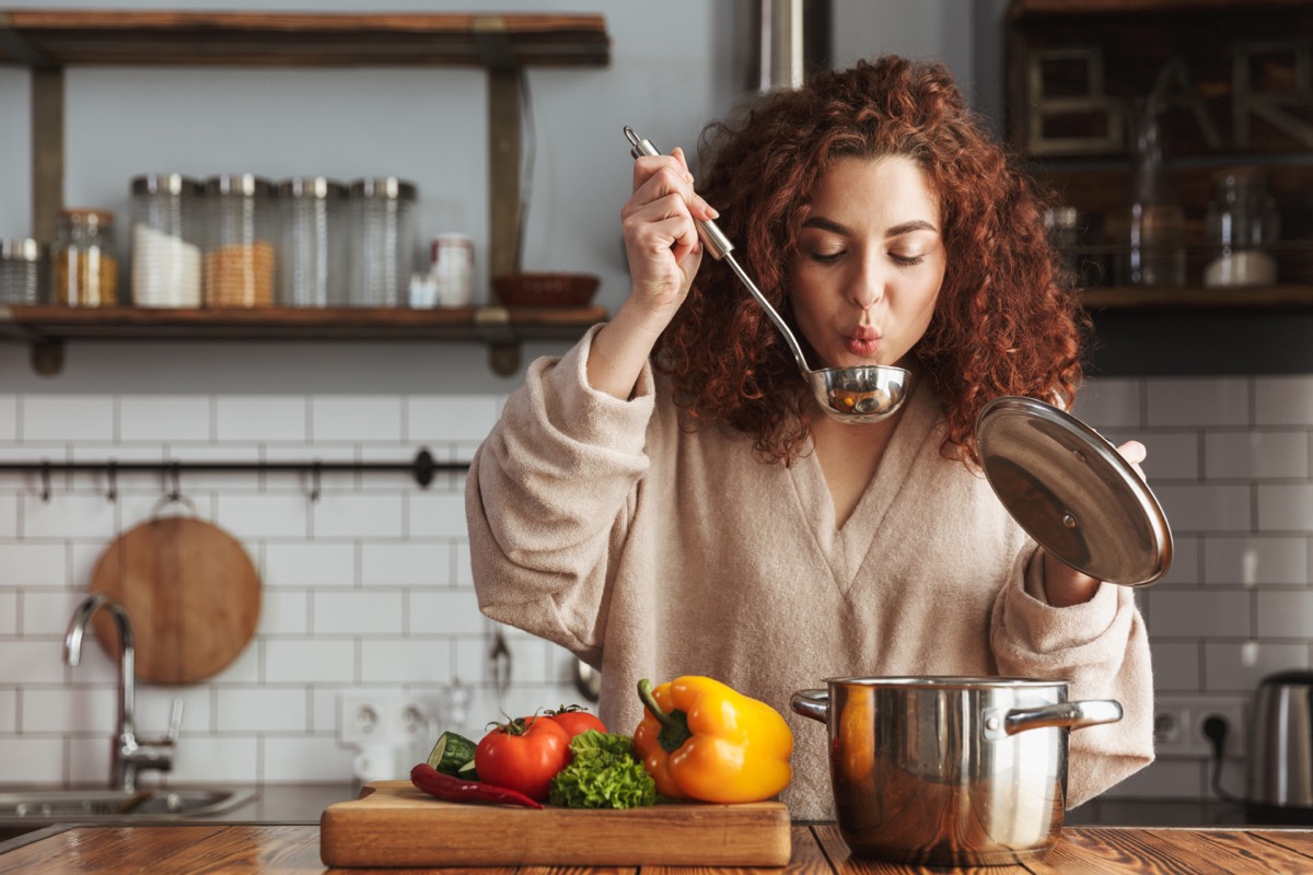 young woman with curly hair blowing on metal soup ladle