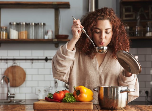 young woman with curly hair blowing on metal soup ladle