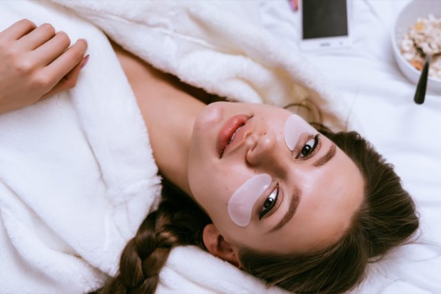 Young girl lies in bed early in the morning, next to a plate of oatmeal porridge, under the eyes of white patches.