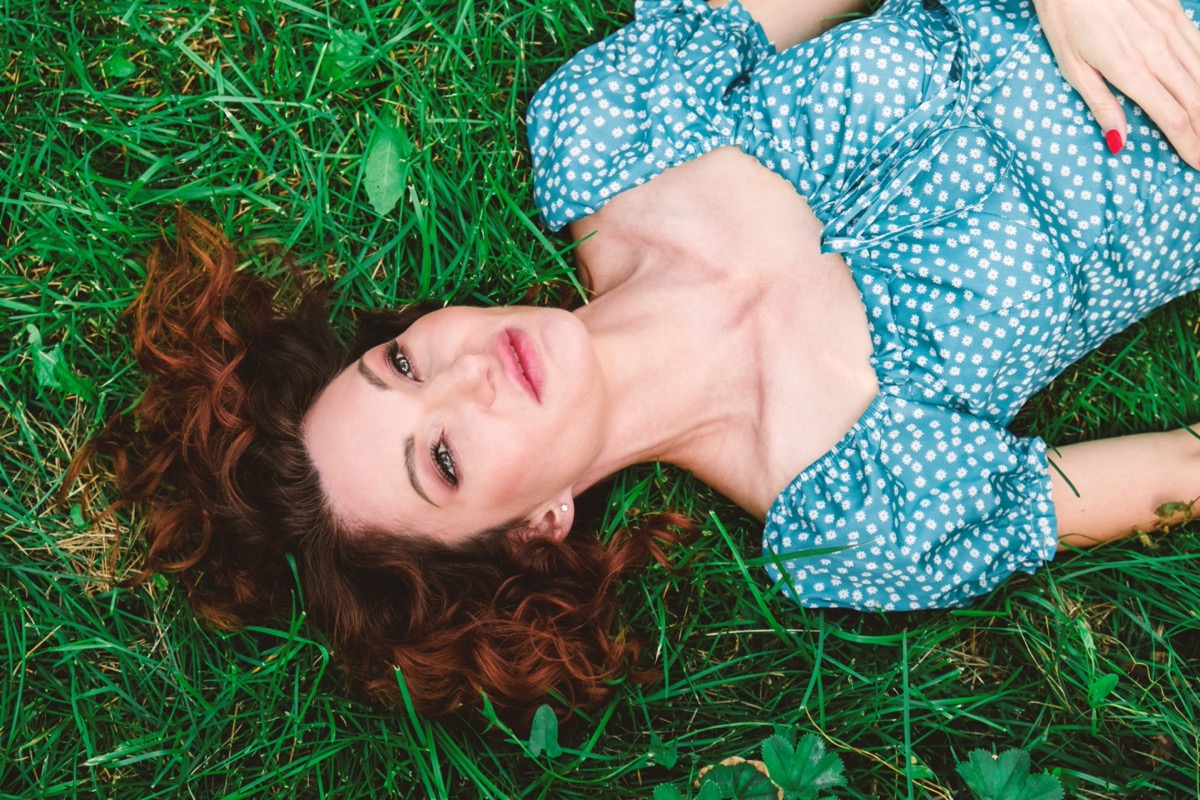 woman lies on green grass with loose red hair