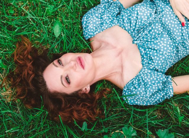 woman lies on green grass with loose red hair