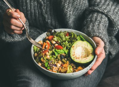 woman holding bowl of salad, avocado, grains, beans, and veggies