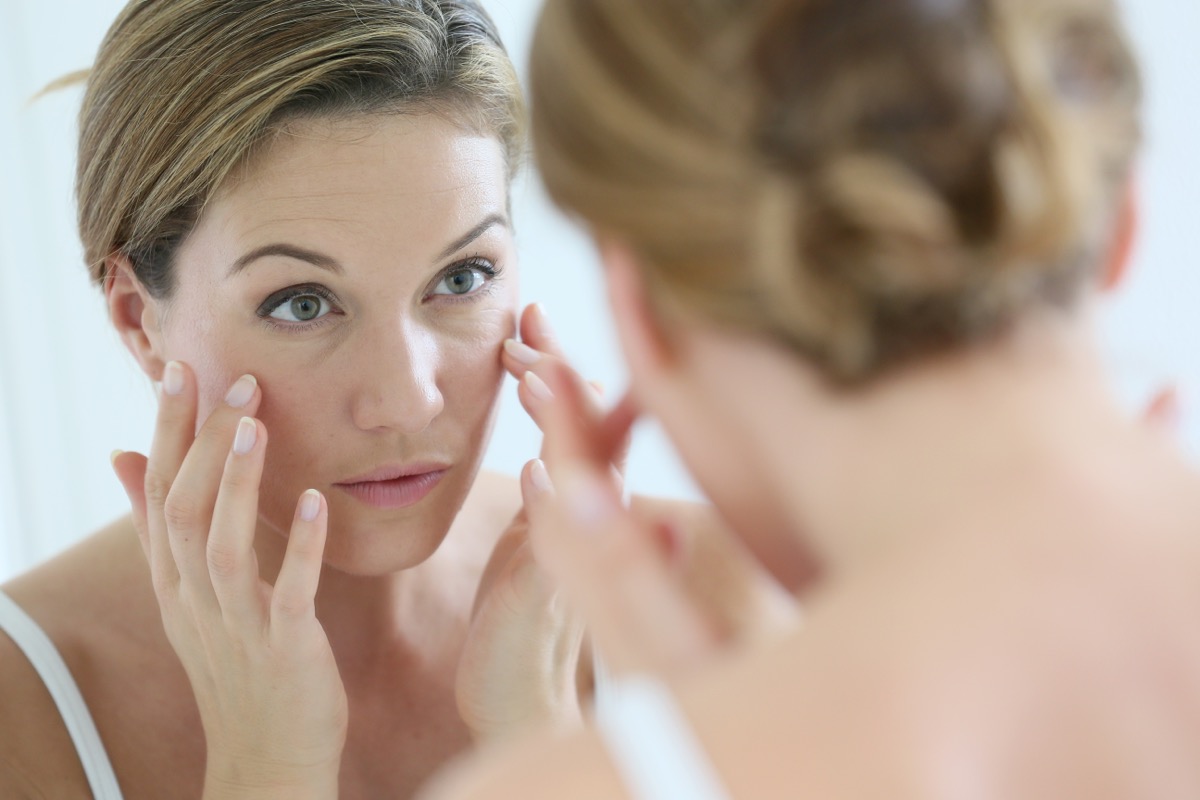 middle-aged blonde woman looking in mirror at wrinkles