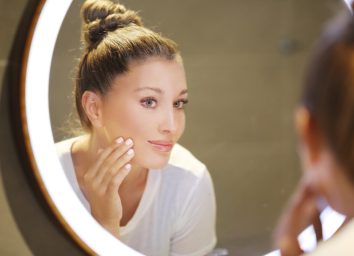 Woman applying face cream in front of the vanity mirror.