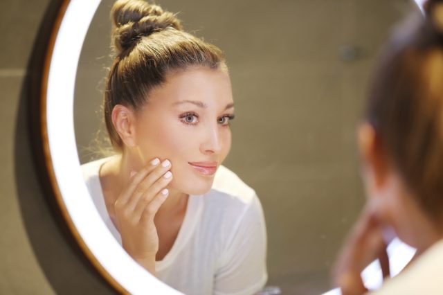 Woman applying face cream in front of the vanity mirror.