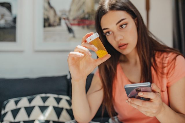 Woman is holding a mobile phone and a bottle of pills