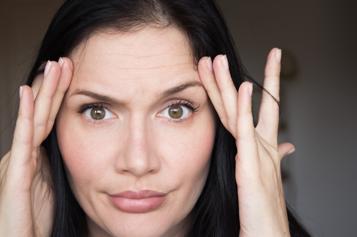 Woman stretching skin on her face and looking at the mirror.