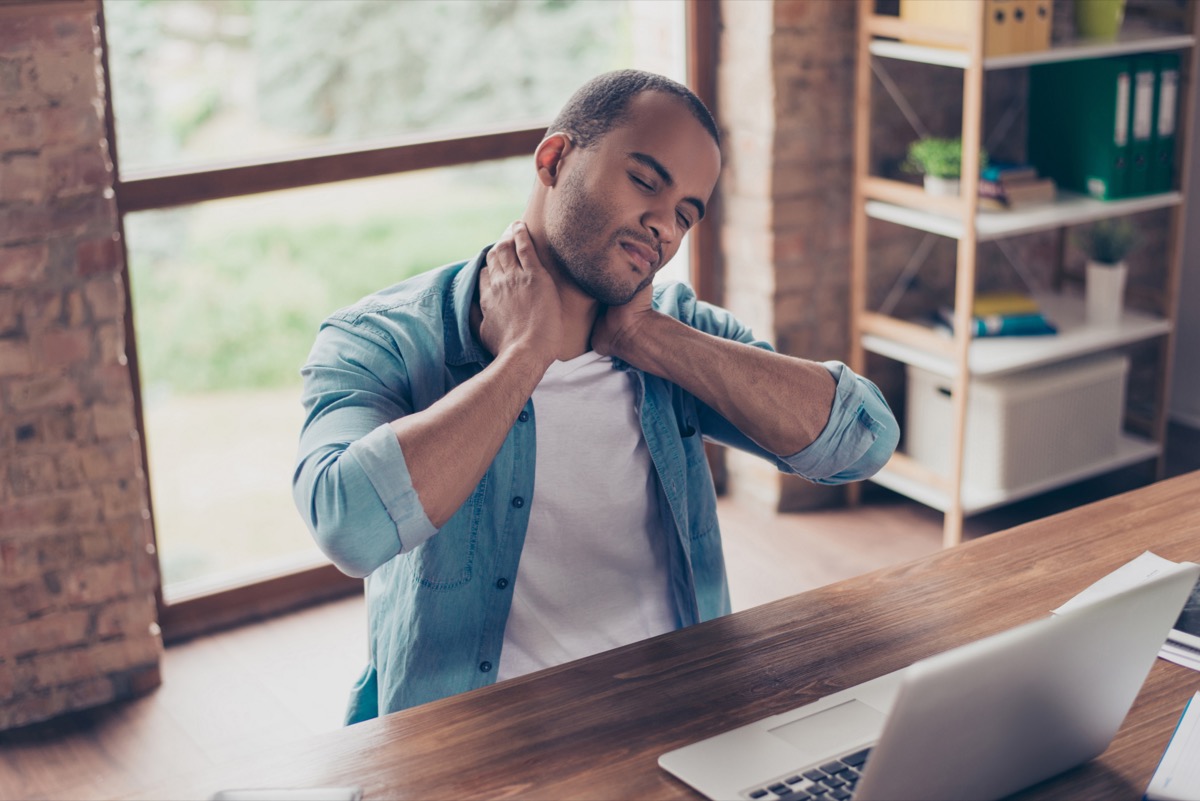 young man with neck pain sitting at desk rubbing neck