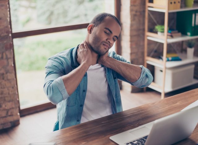 young man with neck pain sitting at desk rubbing neck