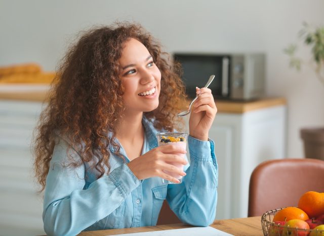 young woman eating yogurt in kitchen