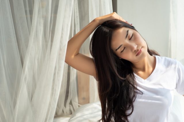 young woman doing neck stretch by window