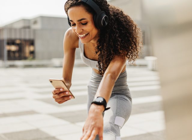 woman looking at her phone while stretching outdoors