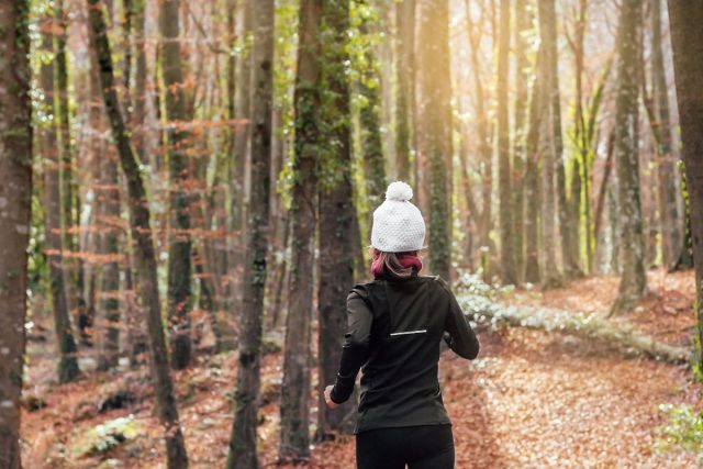 woman bundled up in winter workout attire backwards runs in woods