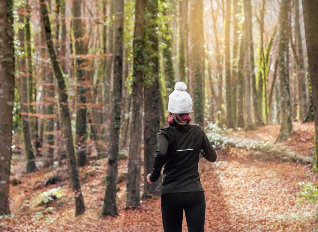 woman bundled up in winter workout attire backwards runs in woods