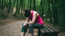 woman in her 30s looks tired as she sits on bench on walking trail