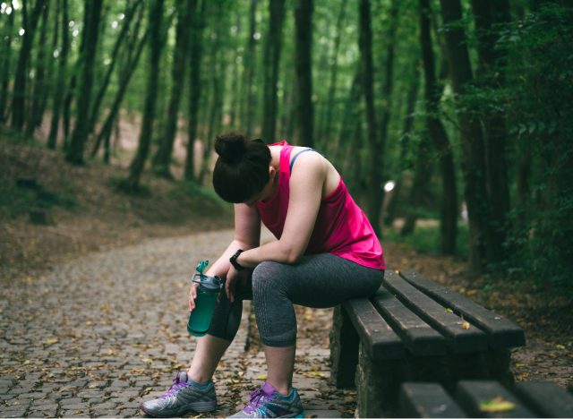 woman in her 30s looks tired as she sits on bench on walking trail