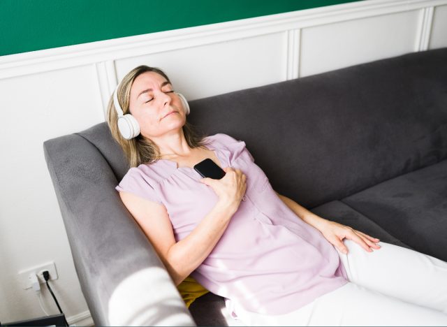 calm woman sits on couch with her eyes closed while listening to music