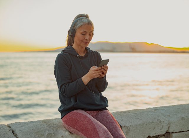 woman in workout attire listens to music on headphones by the beach