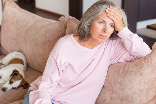unhappy woman sits on couch, hand on forehead