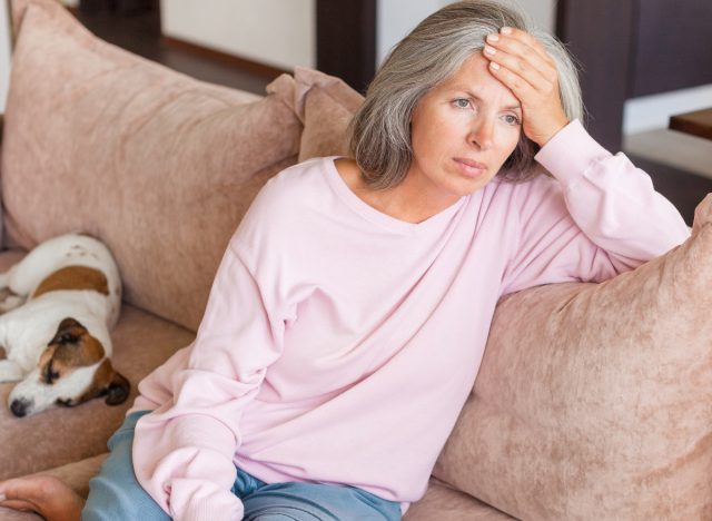 unhappy woman sits on couch, hand on forehead
