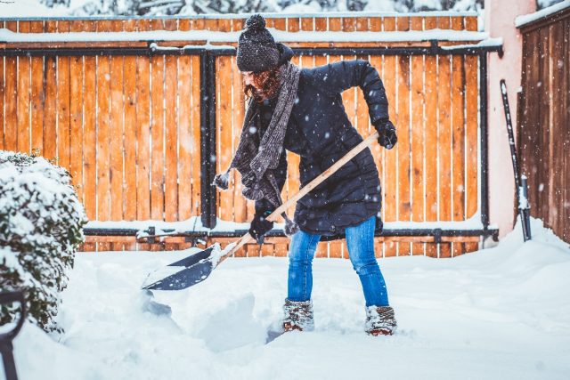 woman shoveling snow in driveway as it snows