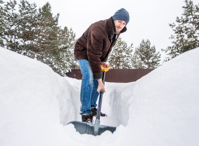 man shoveling pile of snow in driveway