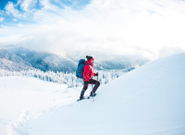 man in red jacket and blue backpack snowshoeing