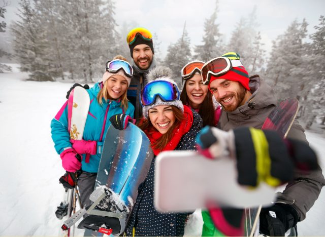 friends who are skiing and snowboarding take a selfie in the snow