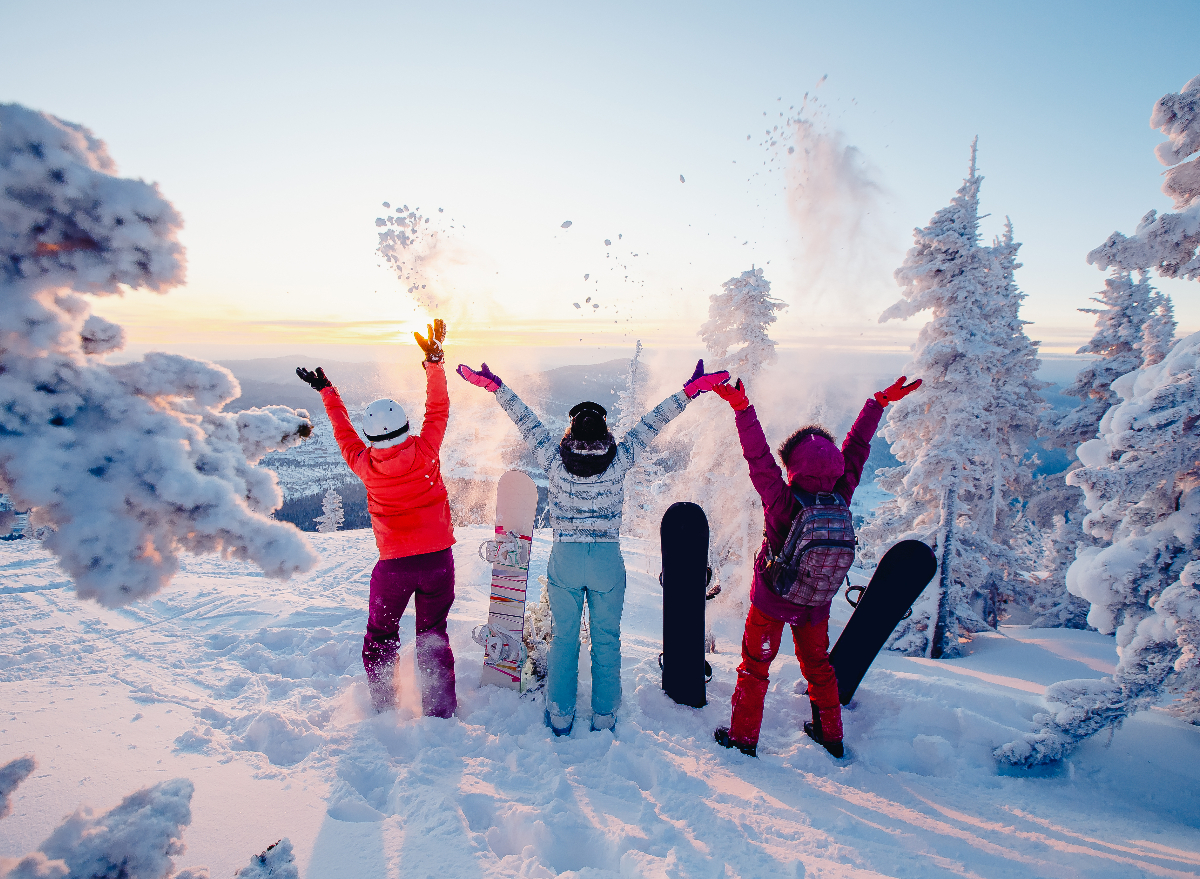 three happy snowboarders toss snow at top of mountain