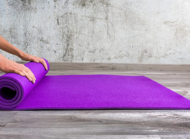 woman's hands rolling out purple yoga mat