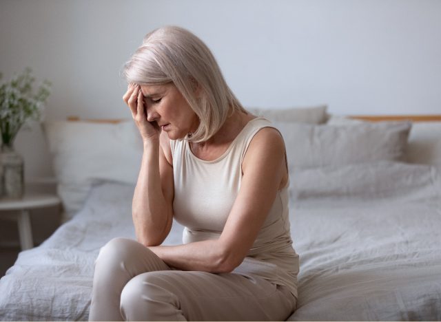 woman rubs her head, tired, sitting on bed